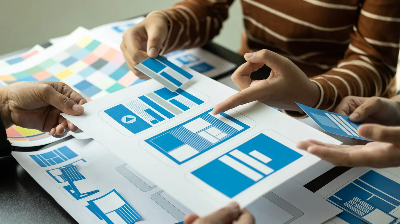 Three people sorting printed blue UI component cards across a shared worksheet
