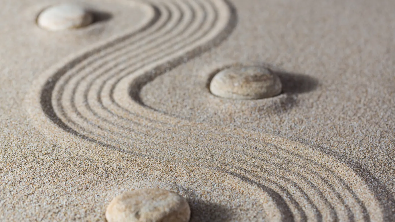 Three smooth stones set into raked sand, an S-curve drawn through the grain around them