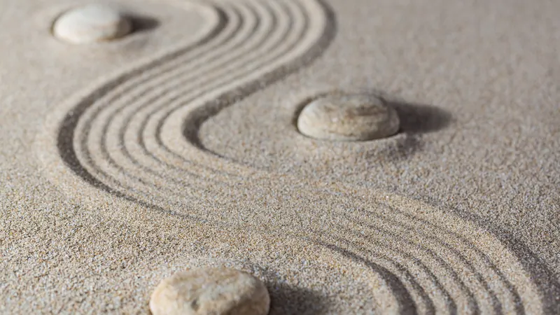 Three smooth stones set into raked sand, an S-curve drawn through the grain around them
