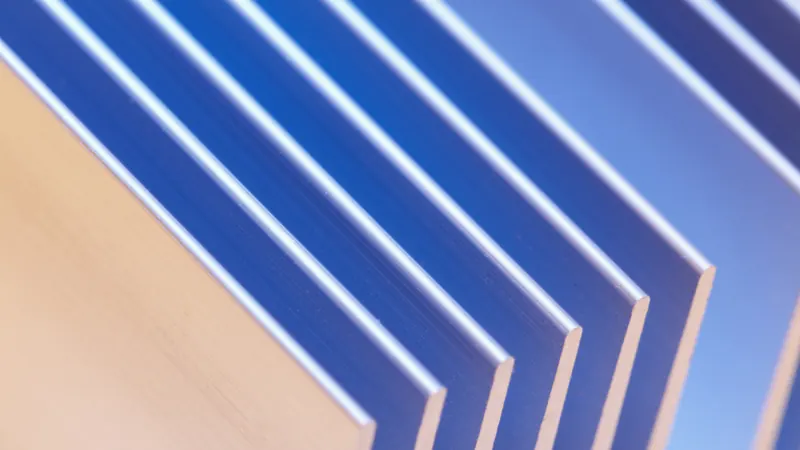 A close-up of stacked aluminium sheets fanned apart, their edges catching blue light